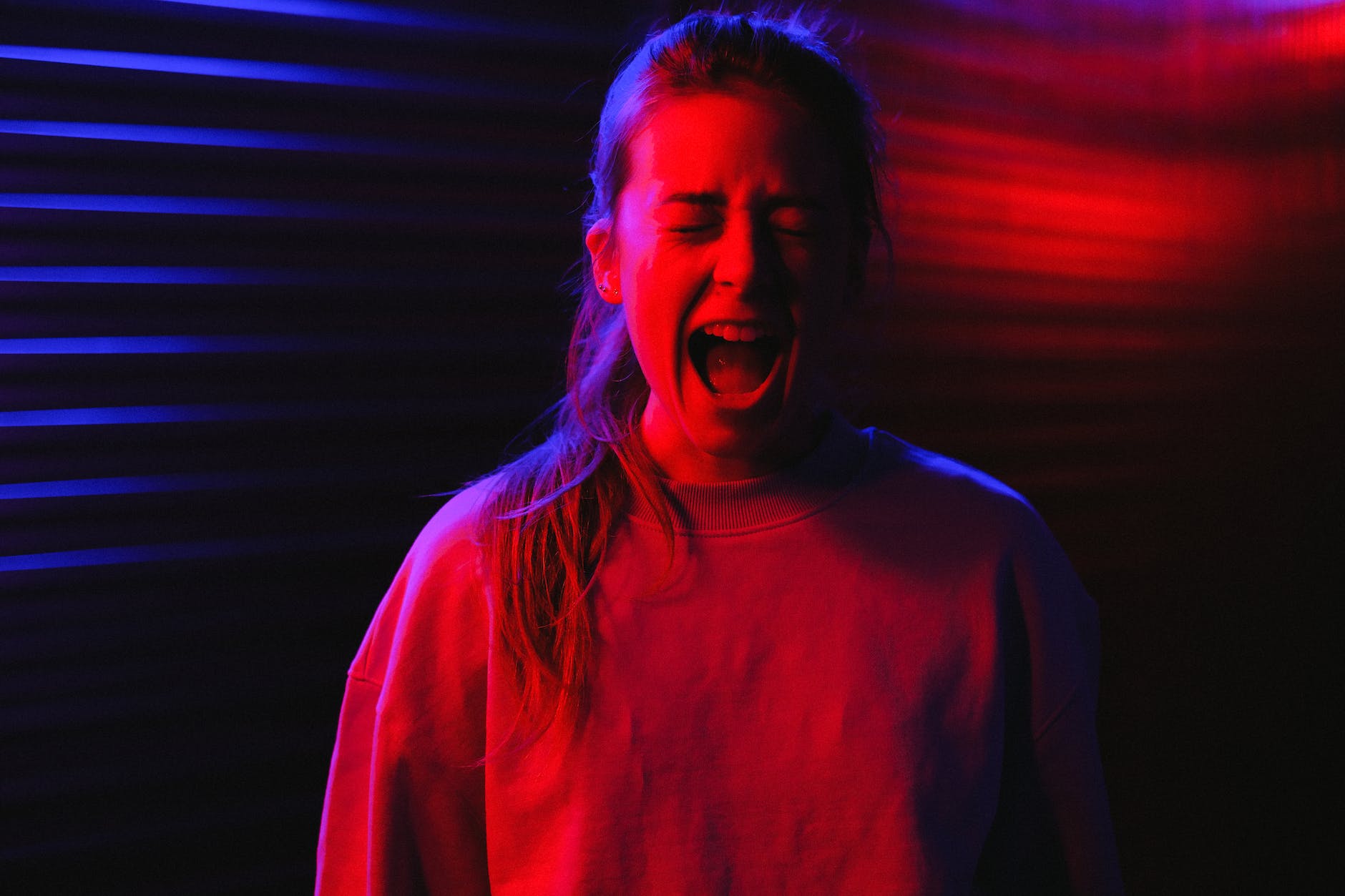 A phot of a young woman screaming with eyes closed depicting a nervous breakdown.