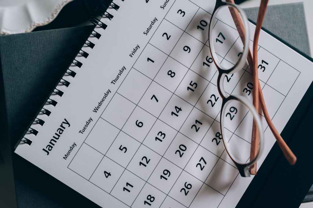 A picture of a month on a calendar sitting on a desk with a pair of glasses resting on top.