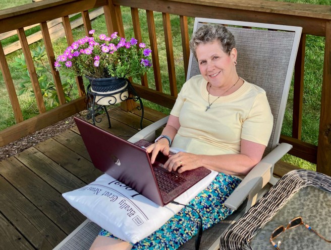 Jackie sitting on her deck with her laptop on a beautiful summer evening writing about hope through chronic illness.